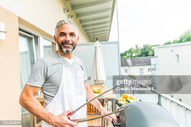 portrait of smiling man with apron and tongs on his balcony - apron stock pictures, royalty-free photos & images