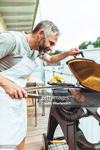 man barbecuing on his balcony - pinça utensílio de servir - fotografias e filmes do acervo