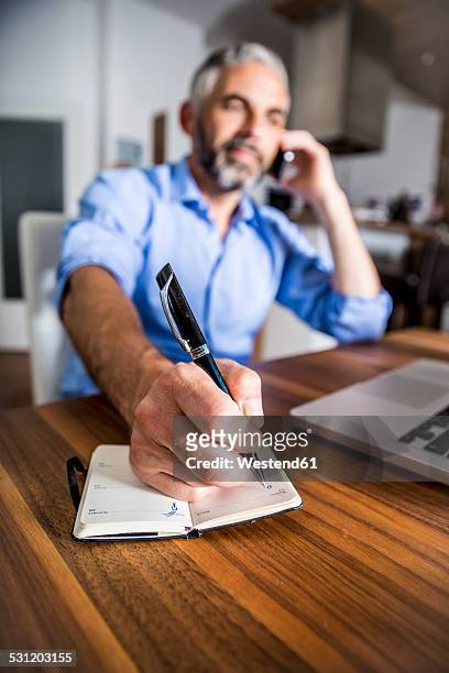 businessman telephoning with his smartphone while making notes - balpen stockfoto's en -beelden