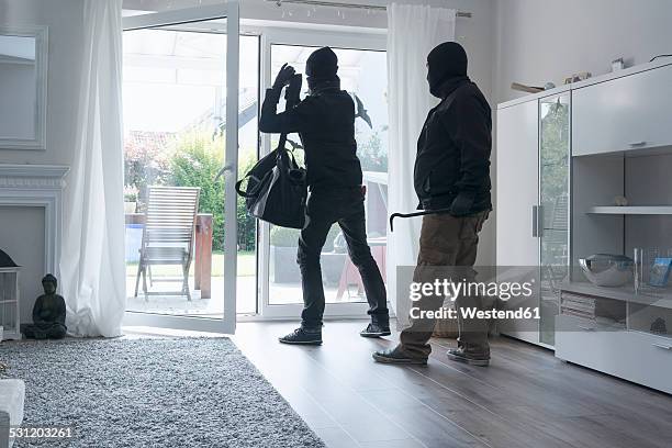 two burglars leaving an one-family house with their loot at daytime - burglary stock pictures, royalty-free photos & images