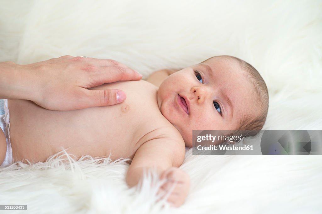 Baby girl lying on sheepskin with mother's hand on the belly