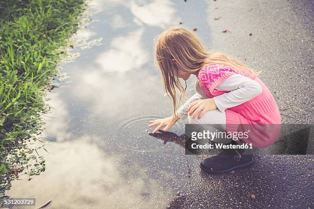 little girl playing with water of a puddle - girls in wet dresses stock-fotos und bilder