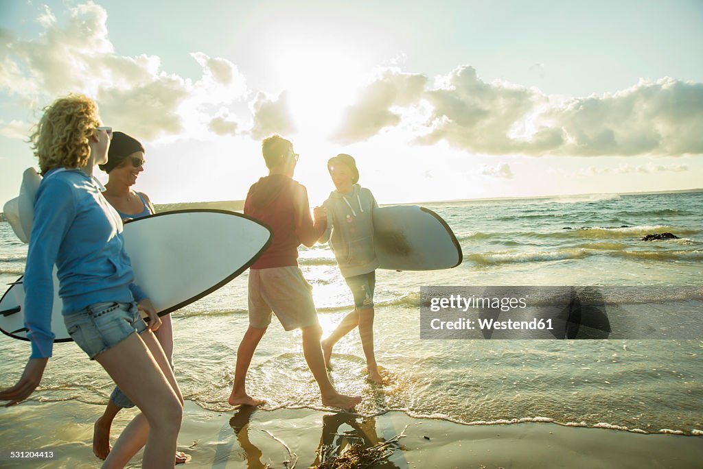 Woman and three teenagers with surfboards walking at waterside of the sea