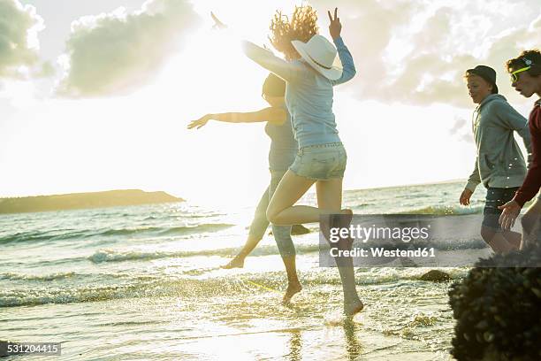 woman and three teenagers having fun on the beach by sunset - boy barefoot rear view stock-fotos und bilder