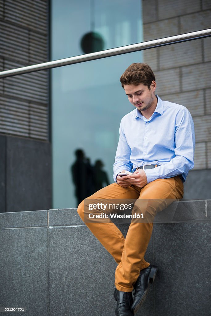 Germany, Hesse, Frankfurt, portrait of sitting young man using his smartphone