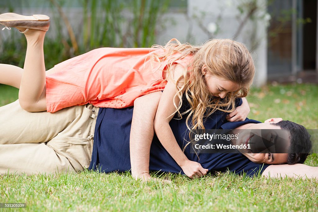 Playful father and daughter lying in grass