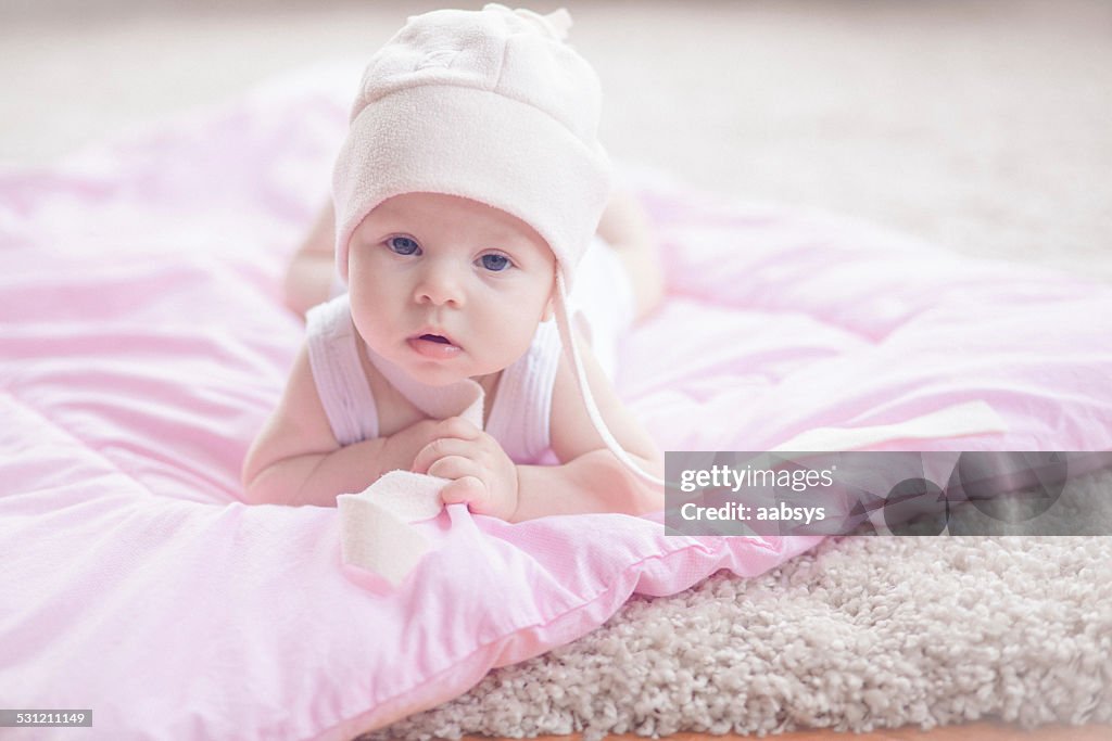 Cute baby girl lying at her stomach looking at camera