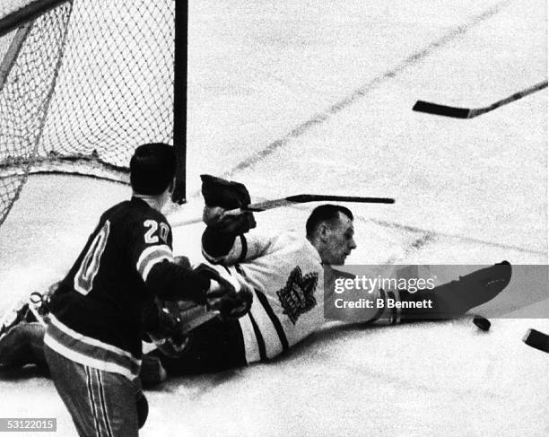 Goalie Johnny Bower looks to make the save, but Reggie Fleming of the New York Rangers pops it in the air to score the Ranger's second goal on...