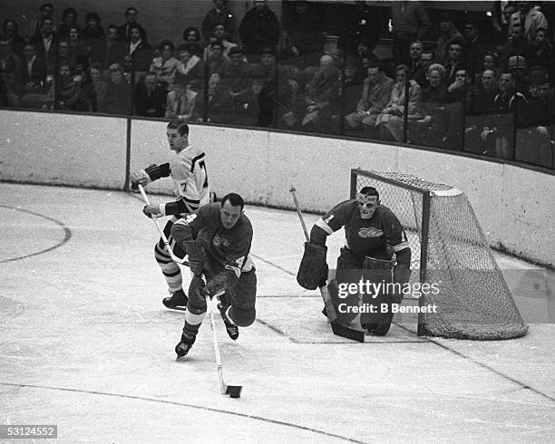 Bill Gadsby of the Detroit Red Wings skates with the puck as his teammate goalie Terry Sawchuk looks on during their game against the Boston Bruins...