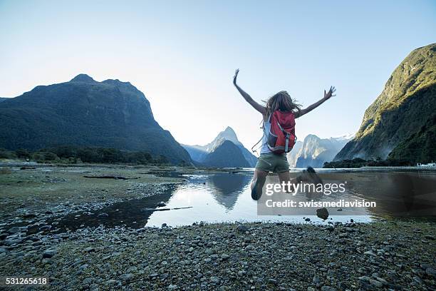 cheering young woman jumps at mitre peak-milford sound, nz - southland new zealand stock pictures, royalty-free photos & images