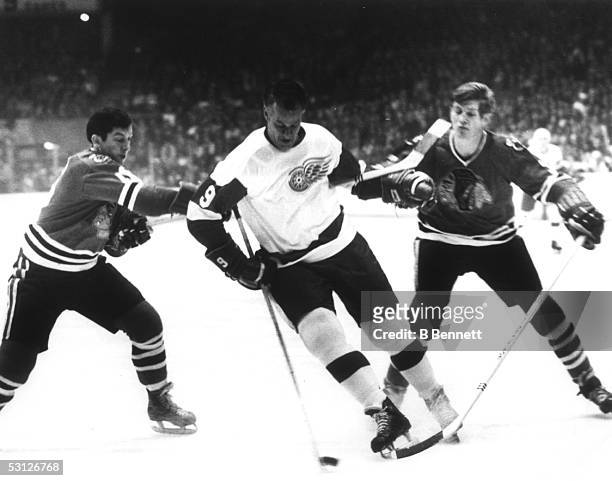 Gordie Howe of the Detroit Red Wings skates with the puck as he battles with Chico Maki and Keith Magnuson of the Chicago Blackhawks during Game 1 of...