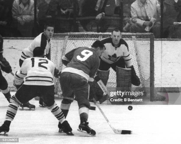 Gordie Howe of the Detroit Red Wings tries to control the bouncing puck in front of goalie Johnny Bower of the Toronto Maple Leafs as Ron Stewart of...