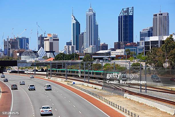 perth cityscape with electric train running down freeway. - perth australia stock pictures, royalty-free photos & images