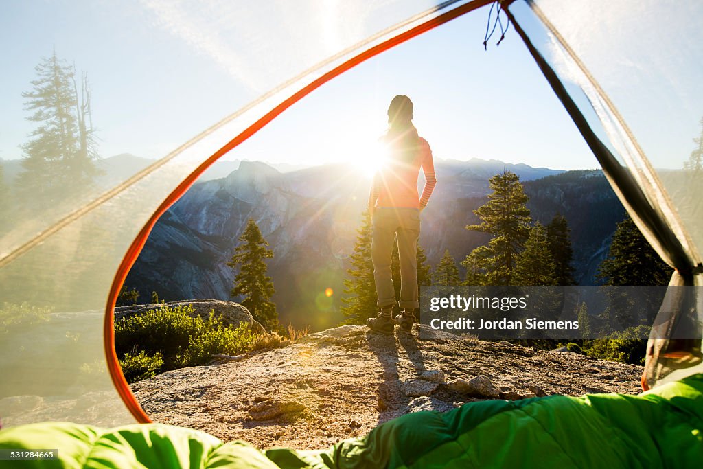 A woman watching sunrise from a tent.