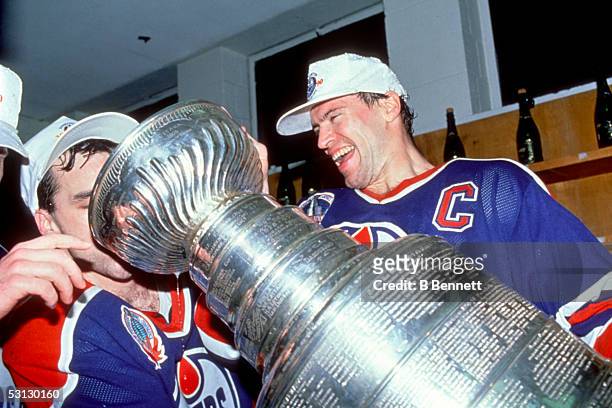 Mark Messier of the Edmonton Oilers helps out teammate Joe Murphy drink from the Stanley Cup in the locker room as they celebrate their Game 5 win...