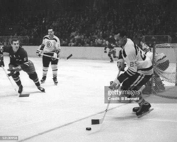Willie O'Ree of the Boston Bruins skates with the puck as Camille Henry of the New York Rangers looks defend during their NHL game circa 1961 at the...