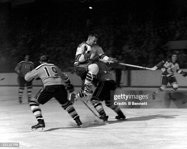Eddie Shack of the New York Rangers leaps through the air between Doug Mohns and Fern Flaman of the Boston Bruins on January 14, 1960 at the Boston...