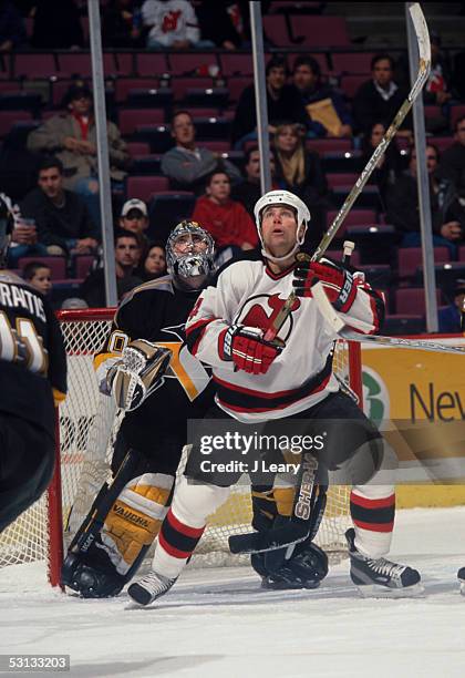 New Jersey's Scott stevens and Pittsburgh goaltender Jean-Sebastien Aubin look up ro see flying puck high above the ice.