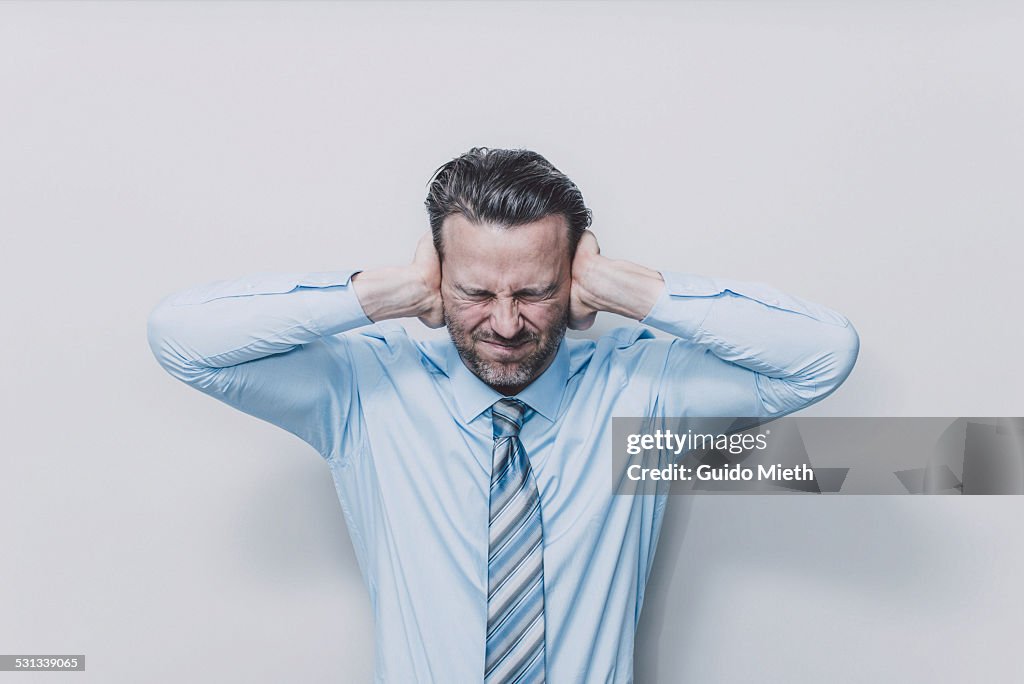 Business man covering his ears.