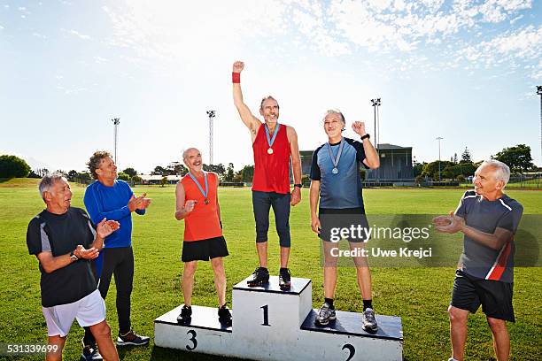 male mature athletes looking at winner on podium - winners podium people stock pictures, royalty-free photos & images