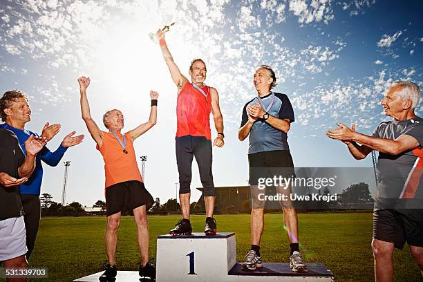 three mature athletes on podium with medals - siegertreppe stock-fotos und bilder