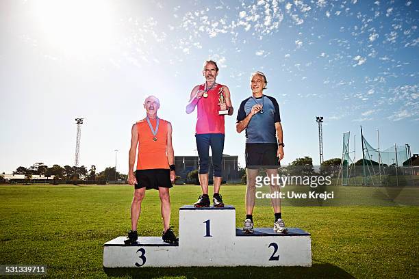 mature male athletes on winners podium - winners podium stock pictures, royalty-free photos & images