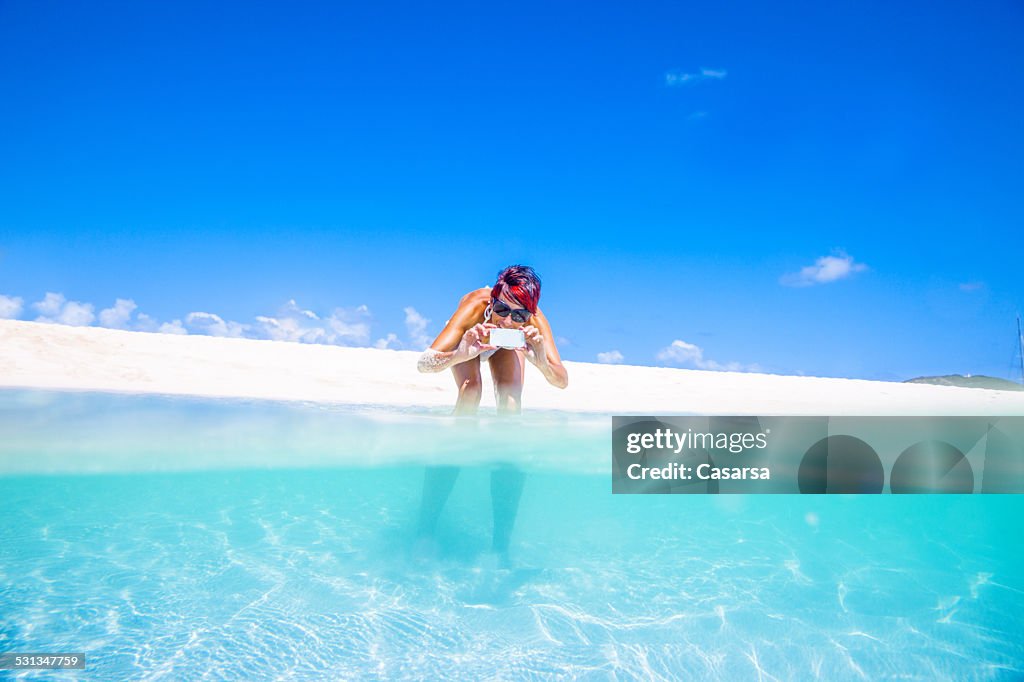 Woman taking images with her smarthone on beautiful beach