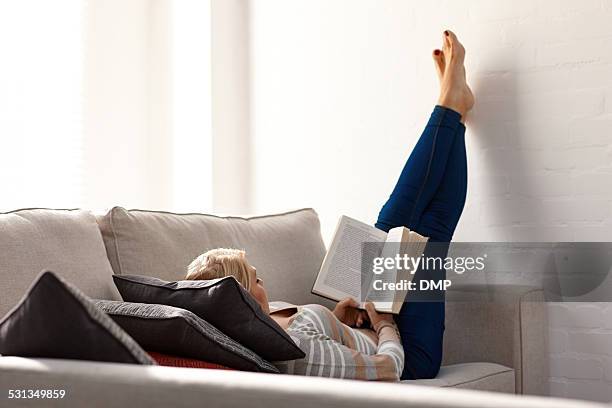 mulher madura relaxante no sofá ler um novo - pés no ar imagens e fotografias de stock