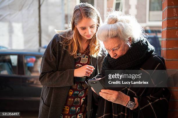 senior lady and grandchild looking at smartphone - senior young woman stockfoto's en -beelden
