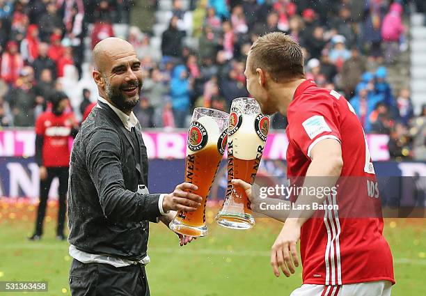 Head coach Josep Guardiola of Bayern Muenchen toast glasses with Holger Badstuber of Bayern Muenchen as they celebrate the Bundesliga champions after...