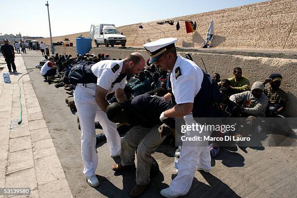 Two Italian Coast Guard Officers tend to an illegal immigrant waiting to be sent to a temporary holding center for foreign nationals on June 21, 2005...