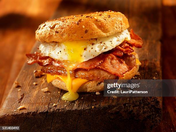 bagel, bacon, sausage and egg breakfast sandwich - spek stockfoto's en -beelden
