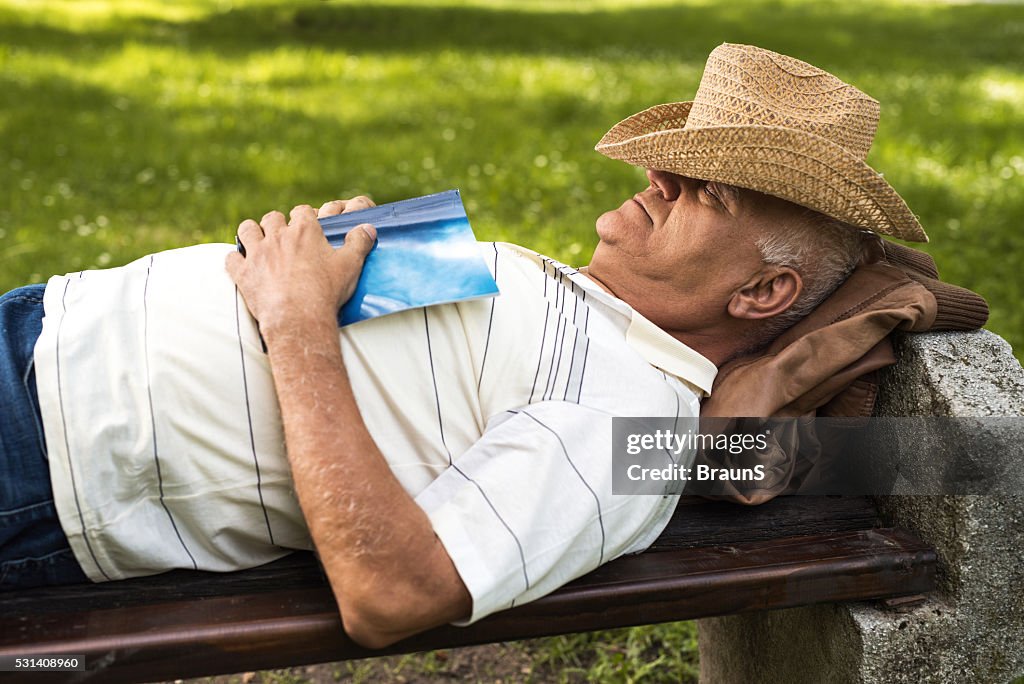 Relaxed senior man taking a nap on a bench outdoors.