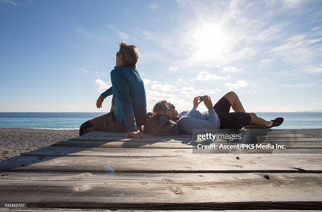 Couple relax on beach wharf, woman sends text