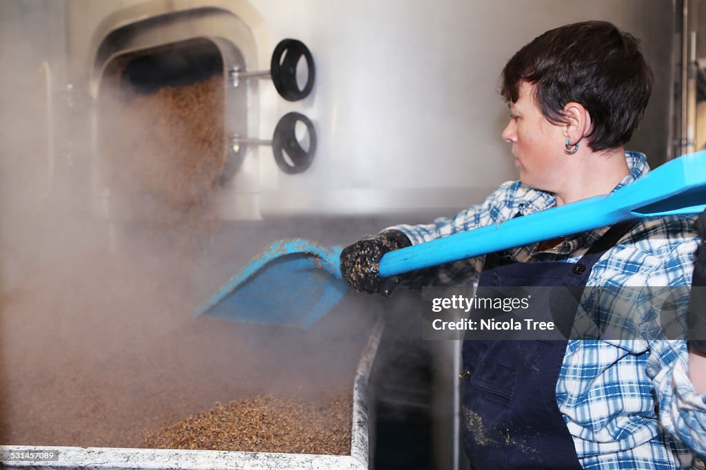 Female brewer emptying grain from tank