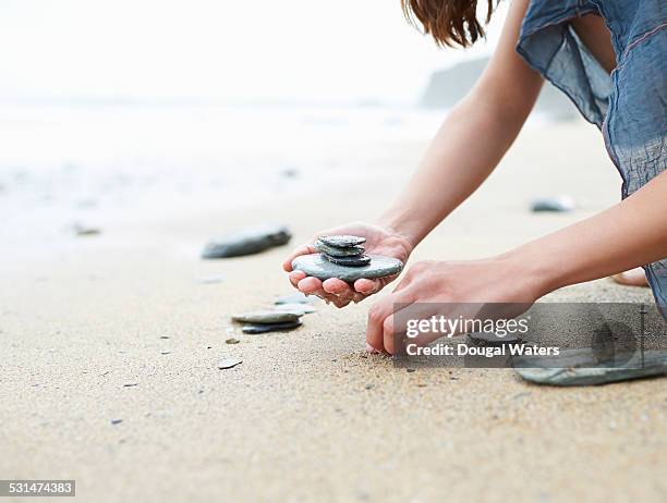 woman collecting small rocks on beach - stone hand stock-fotos und bilder