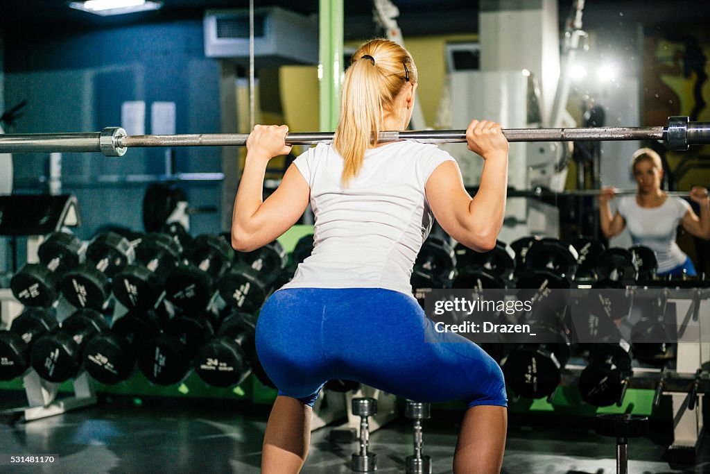 Rubia atleta haciendo se pone en cuclillas en gimnasio para nalga y piernas