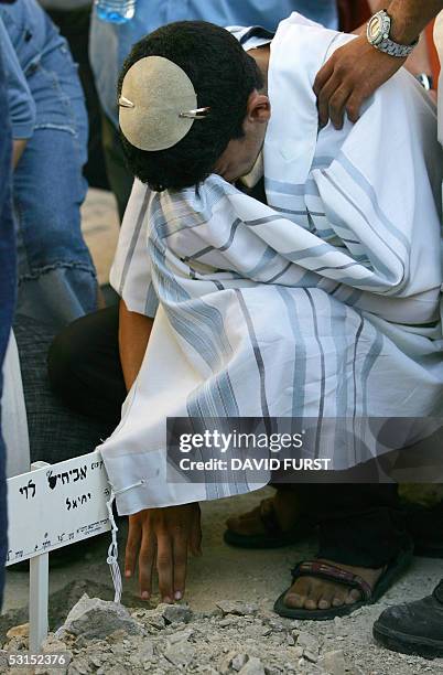 Covered in a traditional Jewish prayer shawl, a mourner weeps over the grave of Avichai Levi from the southern West Bank Settlement of Beit Hagay,...