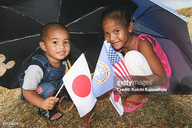 Young supporters hold flags as they shelter under an umbrella during Emperor Akihito and Empress Michiko's visit to their island on June 27, 2005 in...