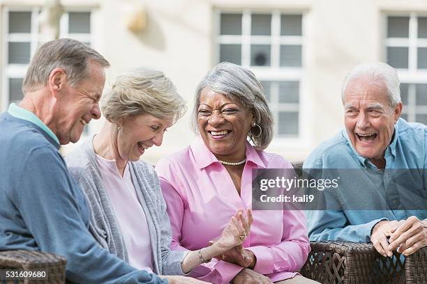 multiracial senior friends sitting outdoors on patio talking - group of seniors stock pictures, royalty-free photos & images