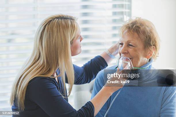 senior mujer, cuidador ayudando con máscara de oxígeno - medical oxygen equipment fotografías e imágenes de stock