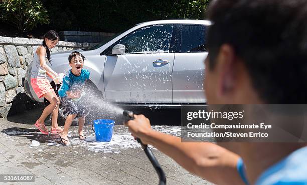 children getting sprayed washing car - two kids playing with hose stock pictures, royalty-free photos & images