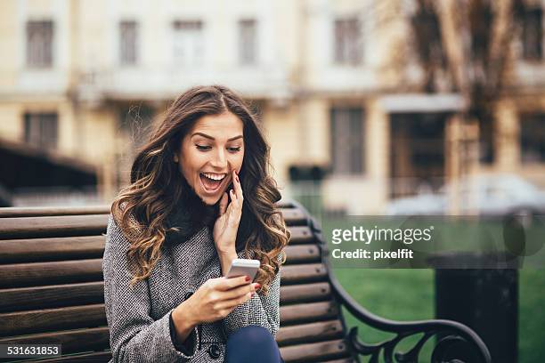 young woman texting on smart phone outdoors - surprised happy woman stock pictures, royalty-free photos & images