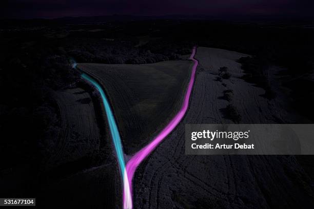 fork road intersection with divergence and flowing trails of light at night in the countryside. - road light trail stock pictures, royalty-free photos & images