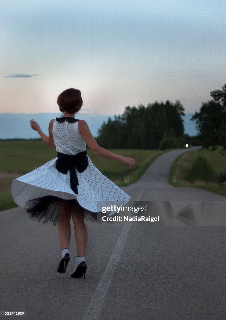 Girl dancing on the road, wearing vintage dress