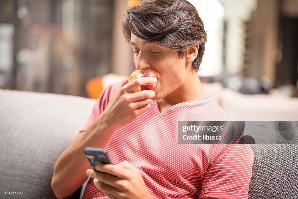 Mann, mit smartphone und isst einen Apfel auf sofa