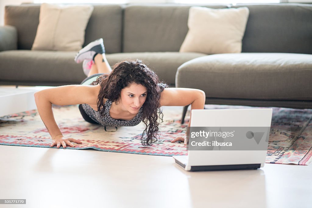 Woman exercising in the living room with laptop