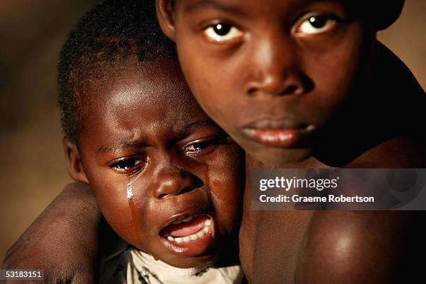 One year old orphan sits on his brother's knee crying in a small village outside Quelimane, on July 2, 2005 in, Mozambique. Since Mozambique's...