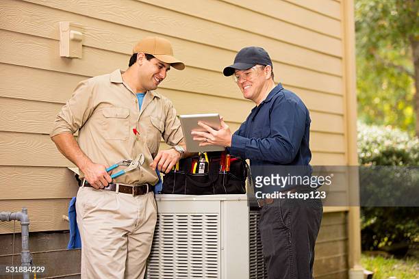 air conditioner repairmen work on home unit. blue collar workers. - air conditioning stock pictures, royalty-free photos & images