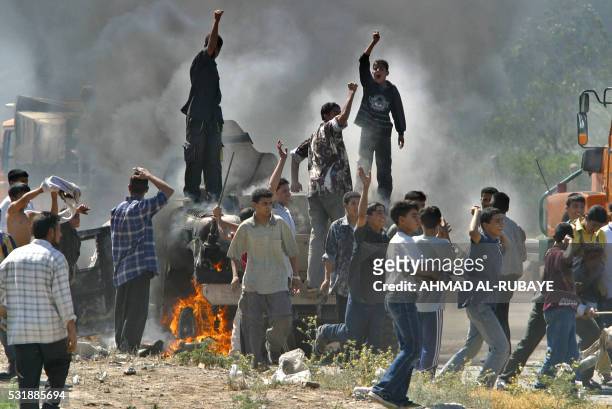 Iraqi children chat anti-US slogans as they loot a burning US Humvee 25 April 2004 on a highway east of Baghdad. The Humvee was abandoned on the...